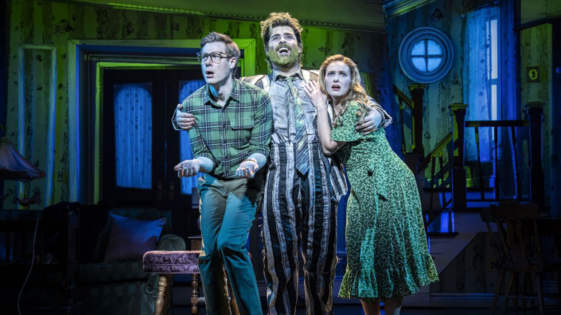 Step into the world of Tim Burton as Beetlejuice the Musical brings the original story to life in a new and imaginative way at the Prince Edward Theatre. Image courtesy of London Theatre Direct. The actor playing Beetlejuice is wearing a stripy black-and-white suit, has green hair and is holding the frightened Maitlands couple.