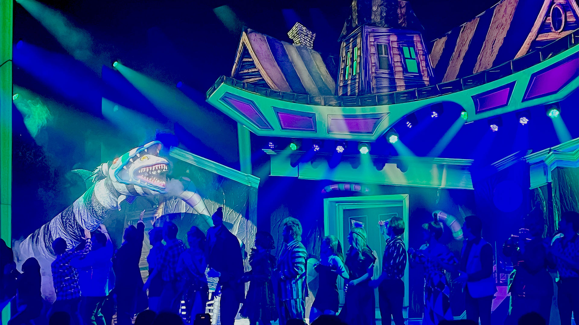 A giant, black-and-white-striped sandworm storms the stage during the curtain call for Beetlejuice the Musical, with a green-and-purple-lit house in the background.