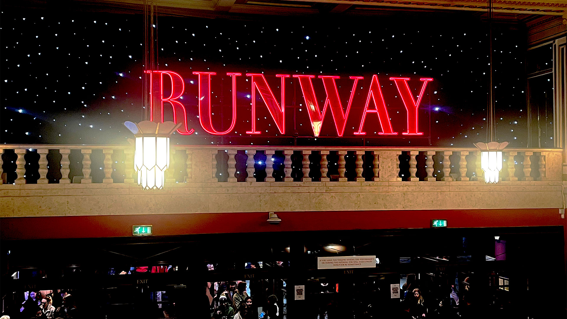 The bright, red, giant neon 'RUNAWAY' sign is perched inside the Dominion Theatre, immersing visitors in the world of The Devil Wears Prada.