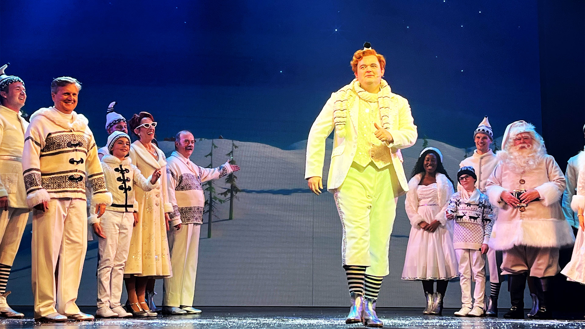 Dressed all in white, Joel Montague, who plays Buddy in ELF, walks past the cast towards the front of the stage.