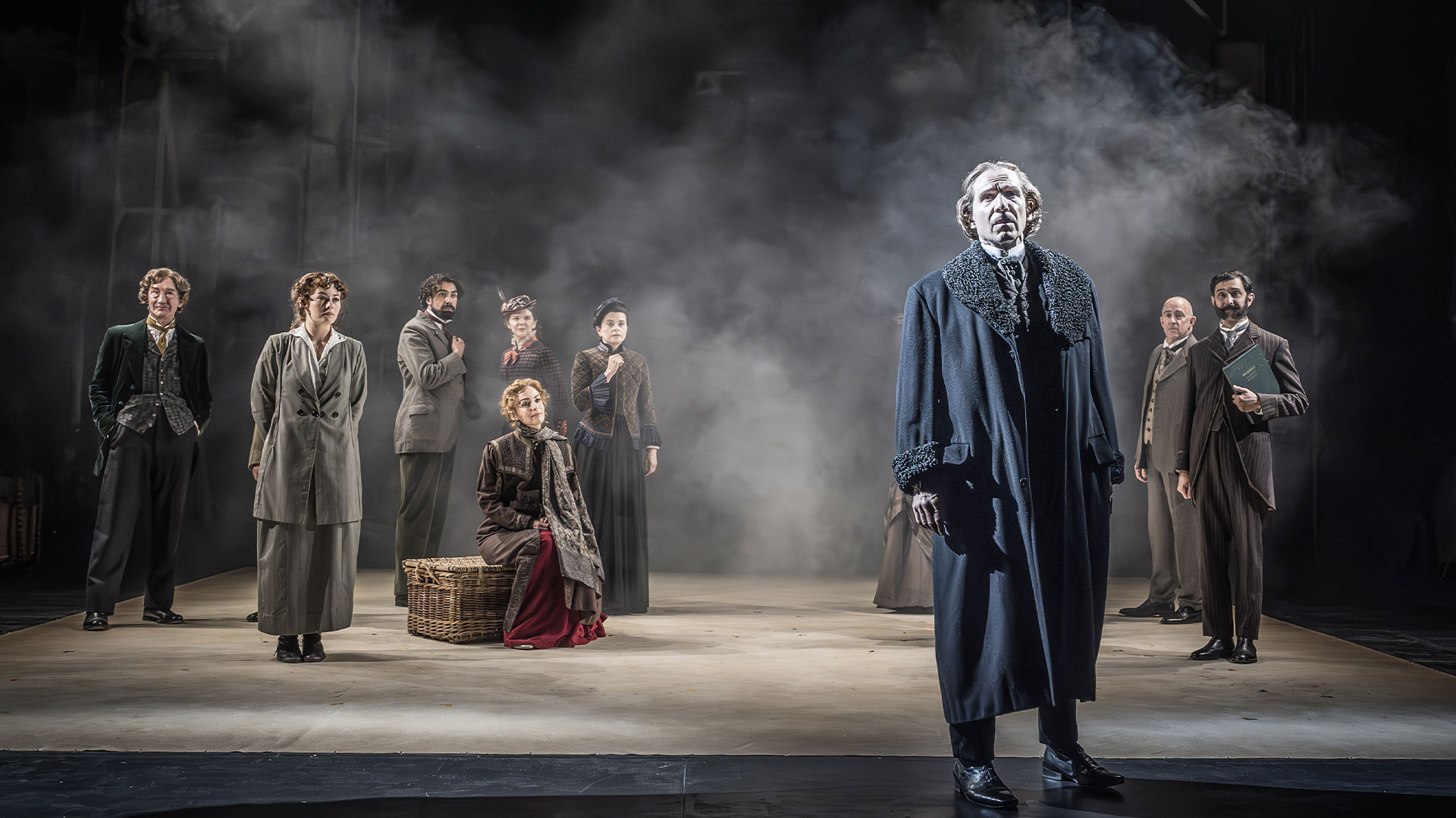 Take a look at the legacy left by Irving and its influence on today's British theatre with the new play Grace Pervades, featuring Ralph Fiennes in the lead role. Image courtesy of London Theatre Direct. Ralph Fiennes stands at the front of the stage wearing a long black coat with other cast members standing at the back surroundded by smoke.