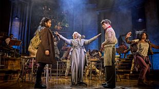 In Hadestown, Malinda Parris plays Hermes, holding her arms up and pointing to the cast members playing Orpheus and Eurydice on stage.