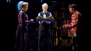 Two boys and a girl stand in the dark around a book, apparently trying out a spell, in a scene from Harry Potter and the Cursed Child.