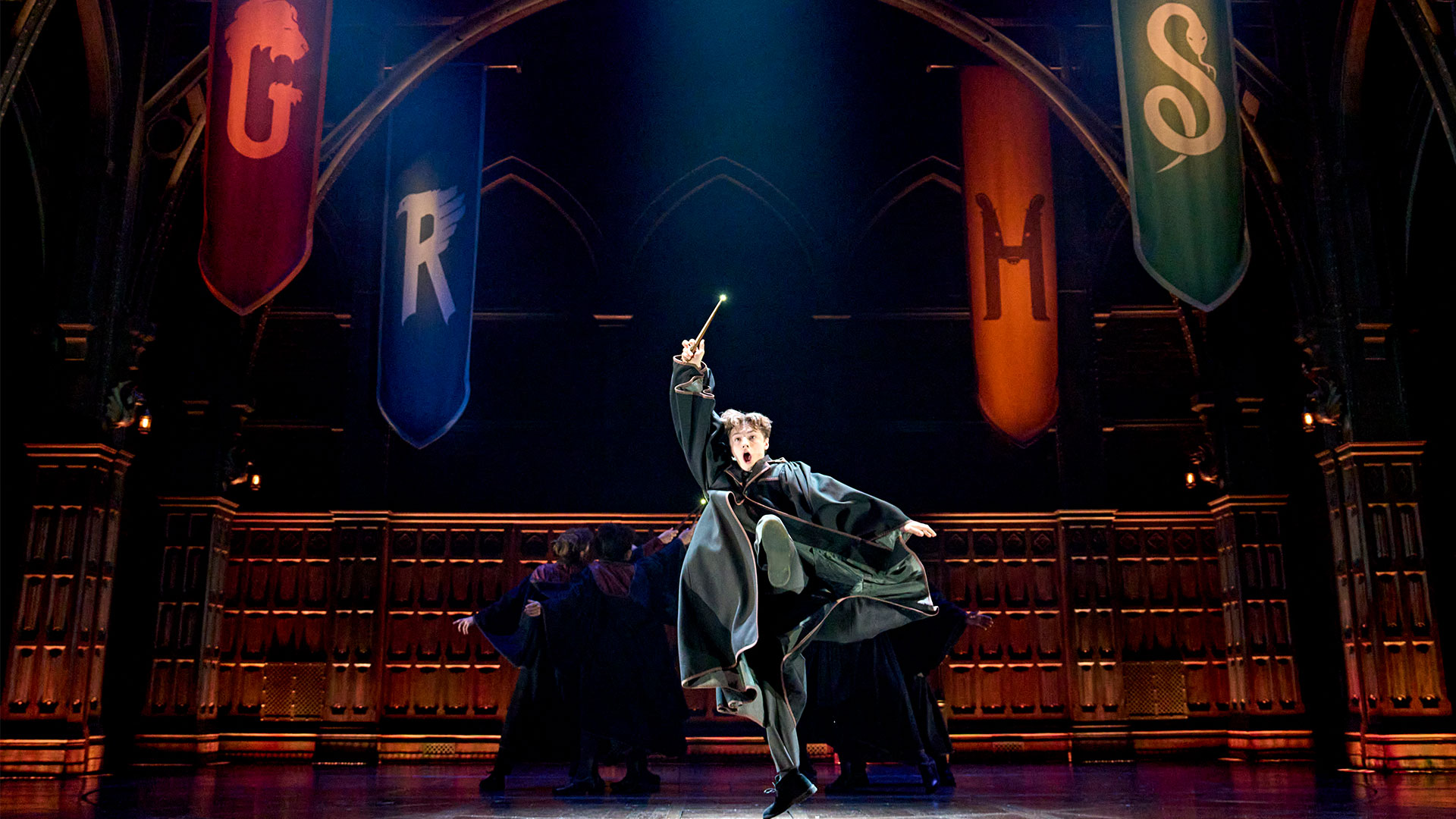 An actor dressed in a wizard's black robe jumps in the air while holding his wand on the stage of Harry Potter and the Cursed Child.
