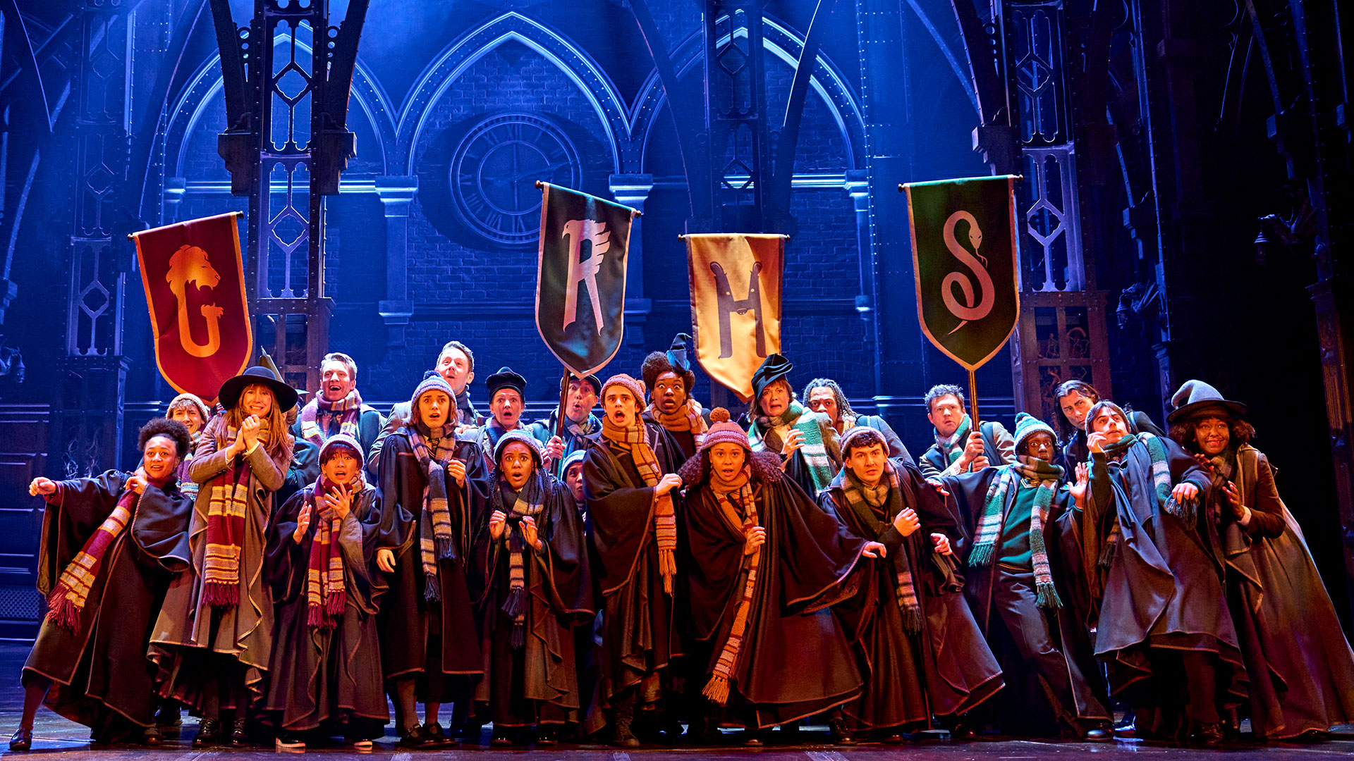 See the spellbinding play currently playing at London's Palace Theatre: Harry Potter and the Cursed Child. ©London Theatre Direct. The cast of Harry Potter and the Cursed Child is on stage, wearing Hogwarts uniforms and holding hight the flags of the school's four houses: Gryffindor, Slytherin, Ravenclaw and Hufflepuff.
