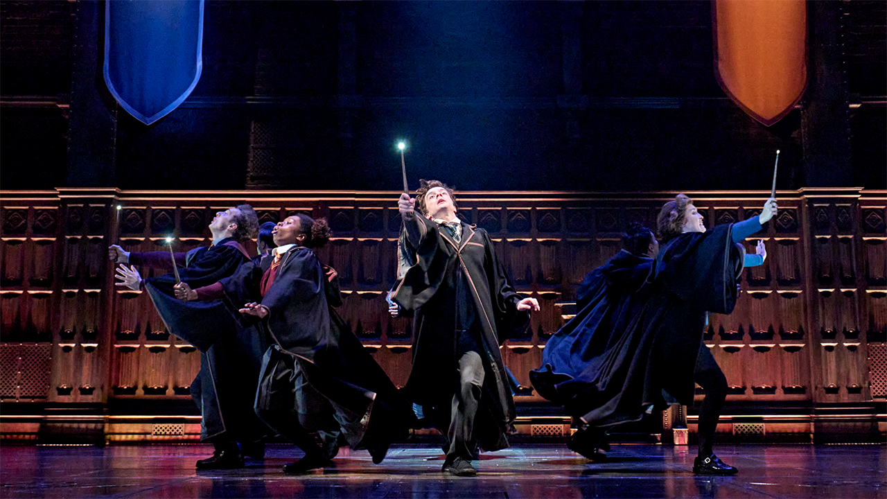 The cast of Harry Potter and the Cursed Child, playing Hogwarts students dressed in their respective uniforms, appear to be locked in a duel armed with their magic wands. 