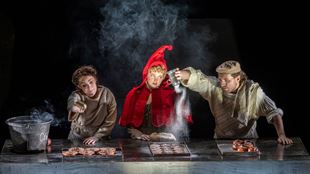 In one scene from Into the Woods, Little Red Riding Hood stands in the middle of the stage, surrounded by the Baker and his wife as they pour sugar over trays of cakes.