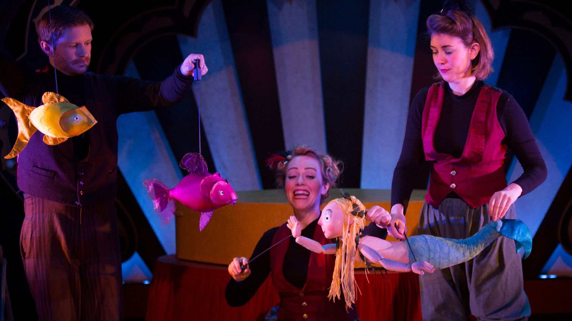 Actors hold puppets on a purple and blue stage at the Little Angel Theatre in London