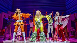 Trois actrices vêtues de costumes colorés de l'époque disco dansent sur la scène de Mamma Mia ! La comédie musicale. 