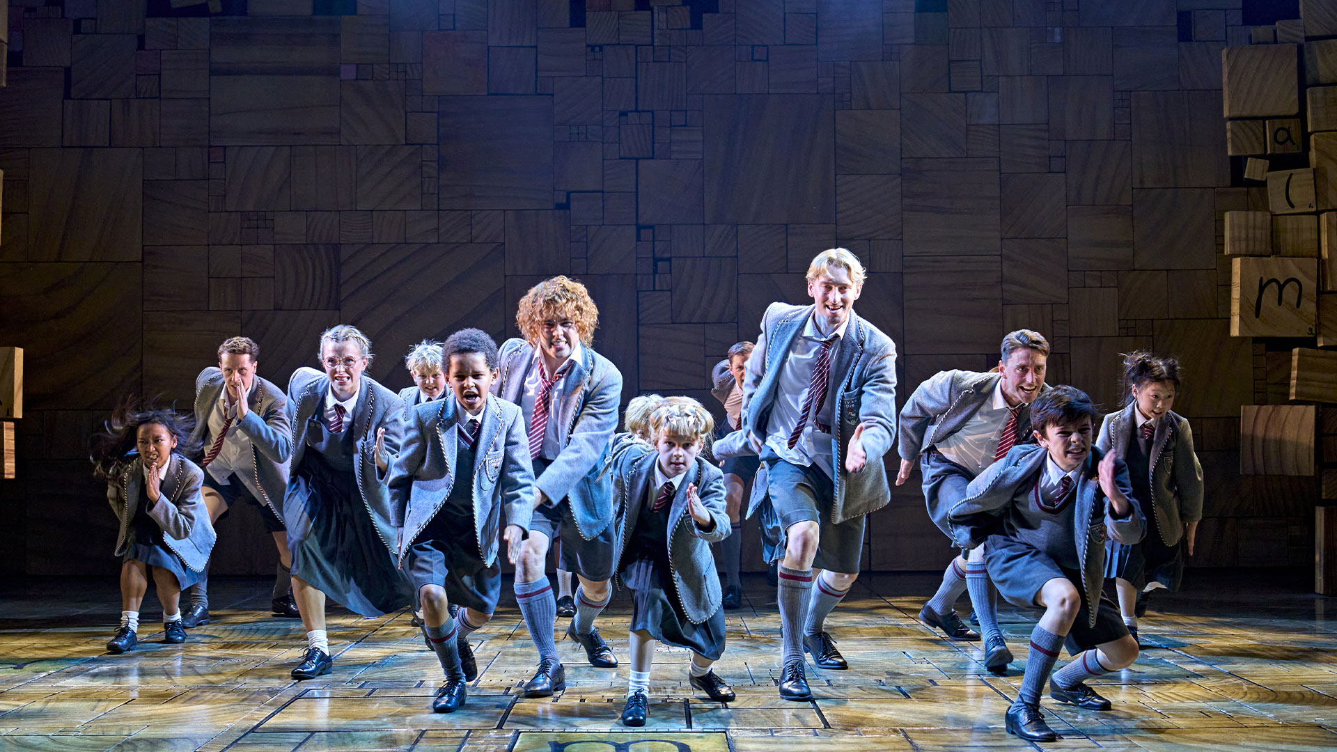 Cast members impersonating schoolchildren in grey uniforms run onto the stage during a scene in Matilda the Musical.