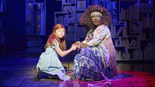 Matilda und die Bibliothekarin sitzen händehaltend auf der Bühne des Cambridge Theaters und schauen das Publikum mit besorgtem Blick an.