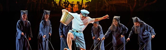 On the stage of My Neighbour Totoro, a man is surrounded by chickens that are moved like puppets by dark figures.