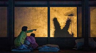 The two actresses playing the roles of Mei and Satsuki are in their bedroom at night, pointing to the window where a strange creature is standing. 