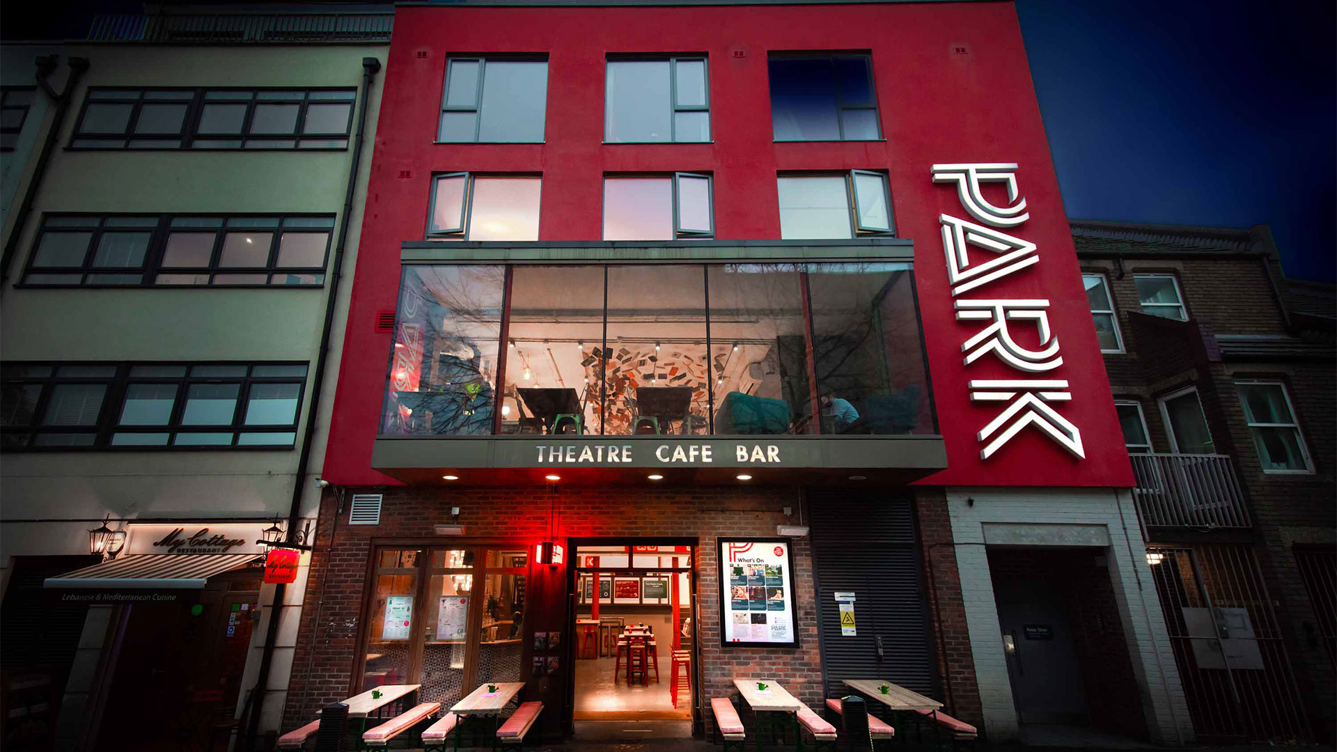 A modern building with a red façade stands with the letters 'Park' on the right-hand side. This is the main entrance to the Park Theatre in London.
