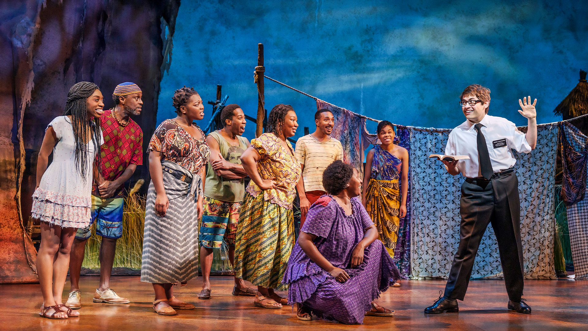 See the award-winning musical The Book of Mormon, currently at the Prince of Wales Theatre. Image courtesy of London Theatre Direct. A Mormon missionary engages with a crowd of people of color on the set of The Book of Mormon.
