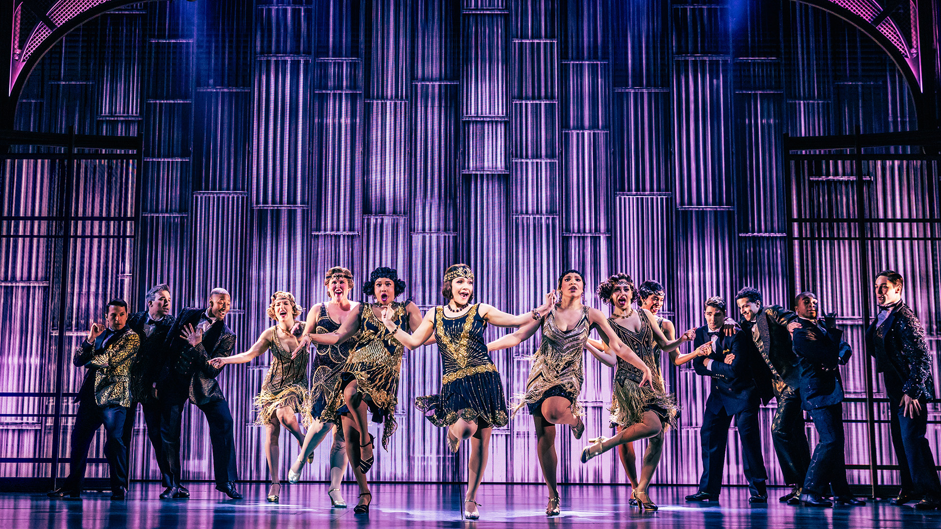 An ensemble perform a dance on stage with the female cast members lit up in the centre.