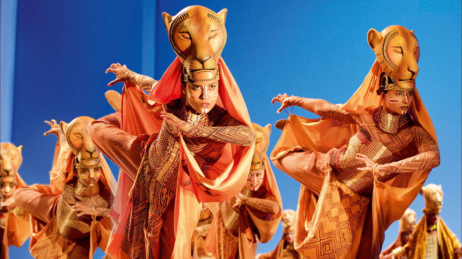 Be mesmerised by stunning costumes and puppetry as some of your favourite characters from Disney's Lion King come to life in London. Image courtesy of Disney/ Photo credit: Van Den Meer. Performers portraying the lionesses in The Lion King musical dance on stage during a hunting scene.