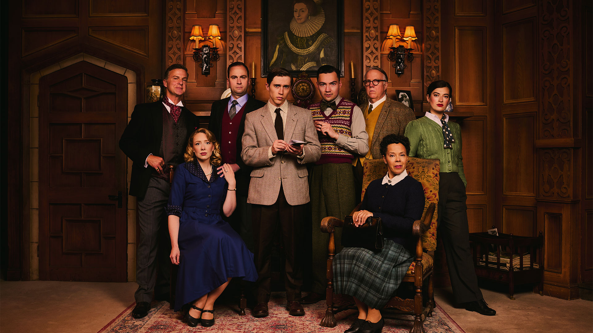 Celebrate 75 years of The Mousetrap with a brand new cast bringing Agatha Christie's story to life. Photo credit: Matt Crockett. The cast of The Mousetrap sit and stand on stage, looking mysteriously at the camera. Two women sit down, and the men stand behind them.