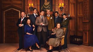 The cast of The Mousetrap sit and stand on stage, looking mysteriously at the camera. Two women sit down, and the men stand behind them.