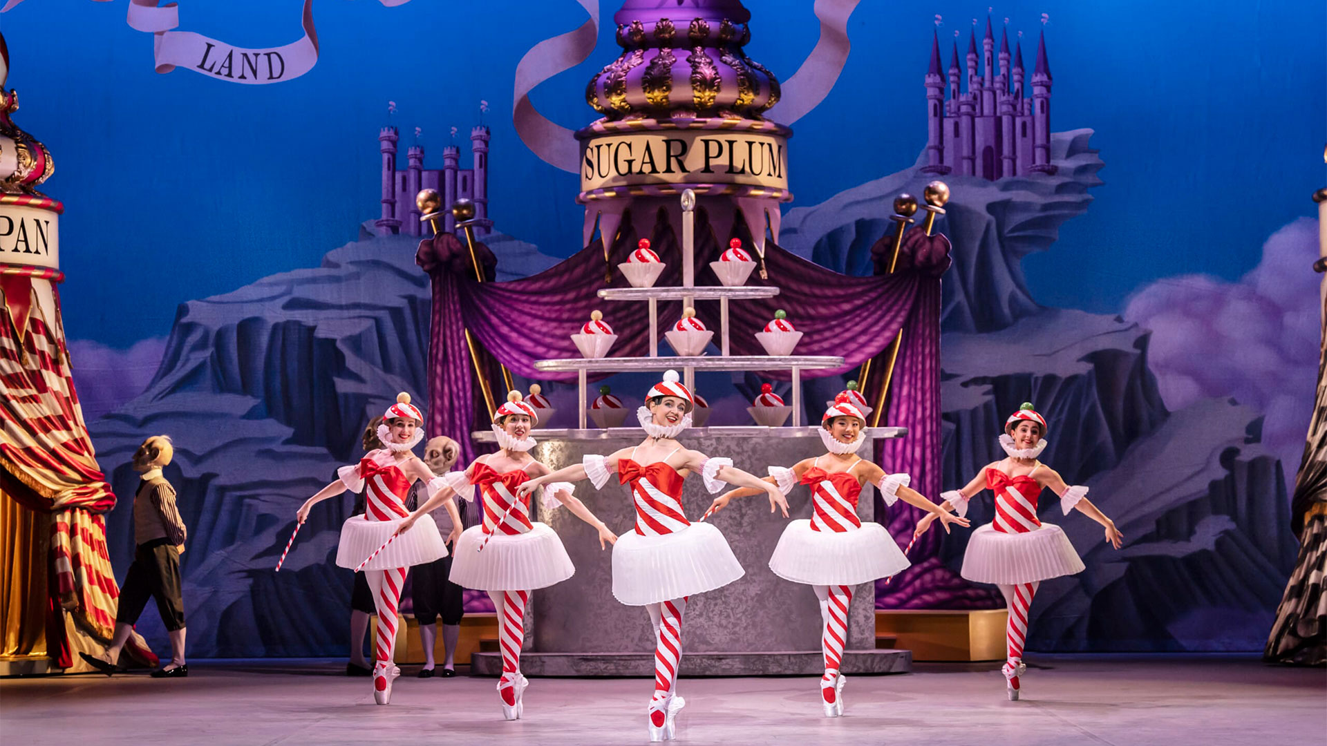 During the production of The Nutcracker Ballet at the London Coliseum, five ballet dancers wearing red and white striped tights and bodices are dancing on stage.