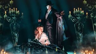The Phantom of the Opera, wearing a mask hiding half of his face, stands above Christine, a young opera singer.