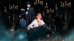 The Phantom of the Opera, wearing a mask hiding half of his face, stands above Christine, a young opera singer.