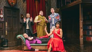 The actors from the Mischief troupe are on stage, dressed in Murder Mystery-style period costumes, looking stunned, their hands raised in defence.