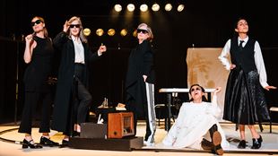 Five actresses are on stage wearing black and white outfits and black sunglasses during a scene in the stage production of The Years.