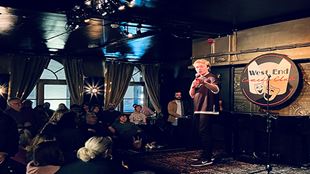 A comedian stands up on stage at the West End Comedy Club.