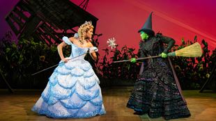 Glida la bonne porte une robe bleu clair et se bat contre Elphaba la méchante sorcière qui brandit son balai.
