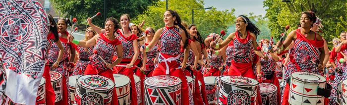 A line up of performers in red outfits bang on drums at notting hill carnival in london.