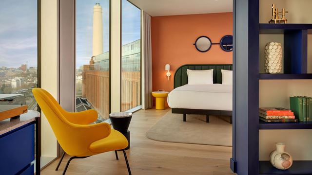 A bedroom filled with colourful furniture and modern artistic touches with floor-to-ceiling windows showing a view of Battersea Power Station in the background