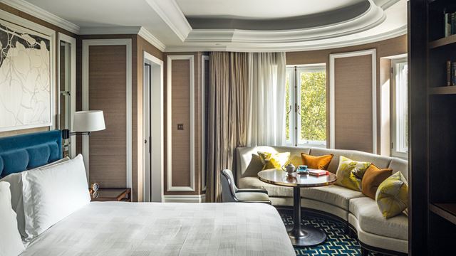 The Park View Corner Suite at The Cadogan, A Belmond Hotel, featuring a curved window and window seat, large bed and traditional style decor.