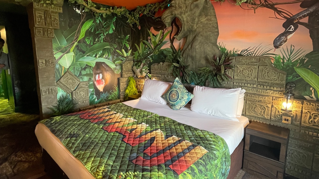 Jumanji-themed hotel room with logo bed covers and jungle wallpaper featuring images of plants and animals