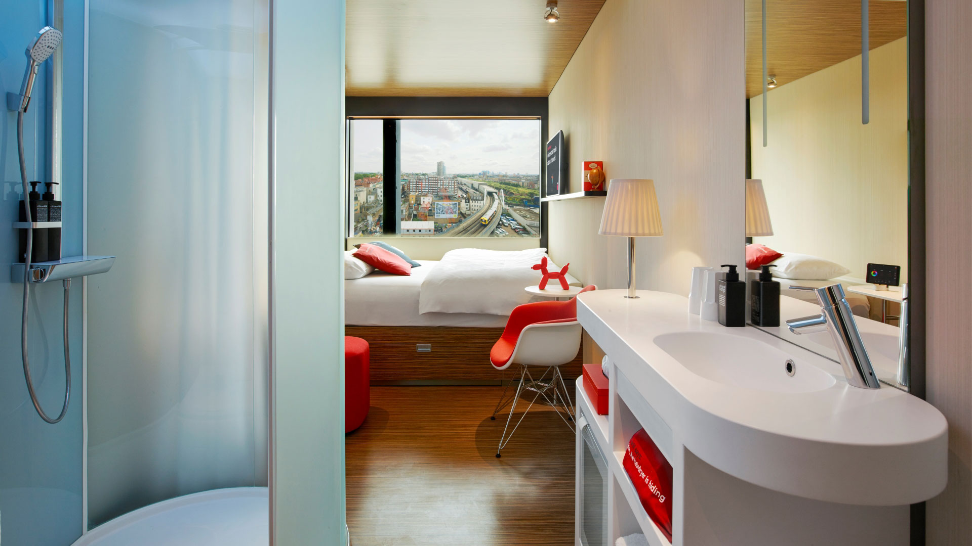 A photo of a room at Citizen M Shoreditch with a giant window with views of London, a desk and large double bed with coloured lights in the shower that can be controlled with in-room technology