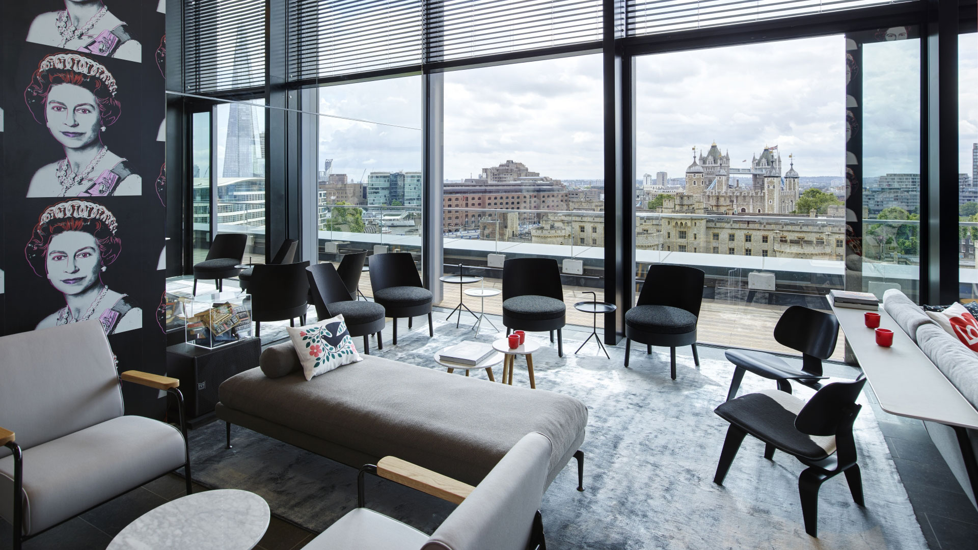 A photo of a communal area at Citizen M Tower of London with comfortable chairs, sofas and pop art imagery on the walls with floor-to-ceiling windows boasting views of the London skyline including The Tower of London and The Shard 