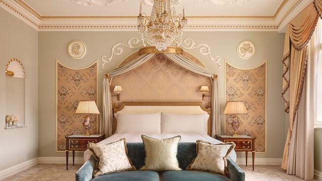 A grand bedroom suite in Claridge's with a green sofa, bed with drapes, and high ceilings featuring elegant cream-coloured mouldings.