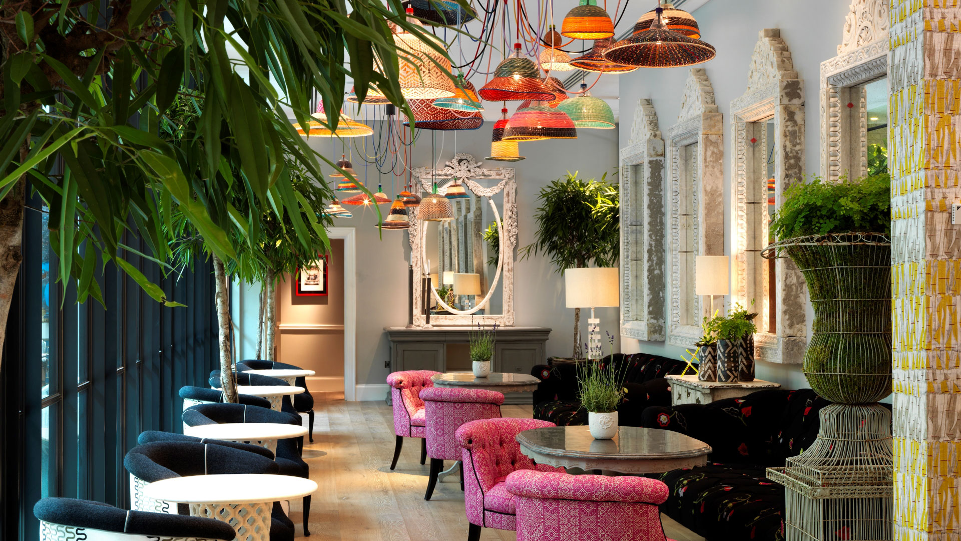 Colourful pendant lamps hang above patterned chairs and tables with plants lining the room