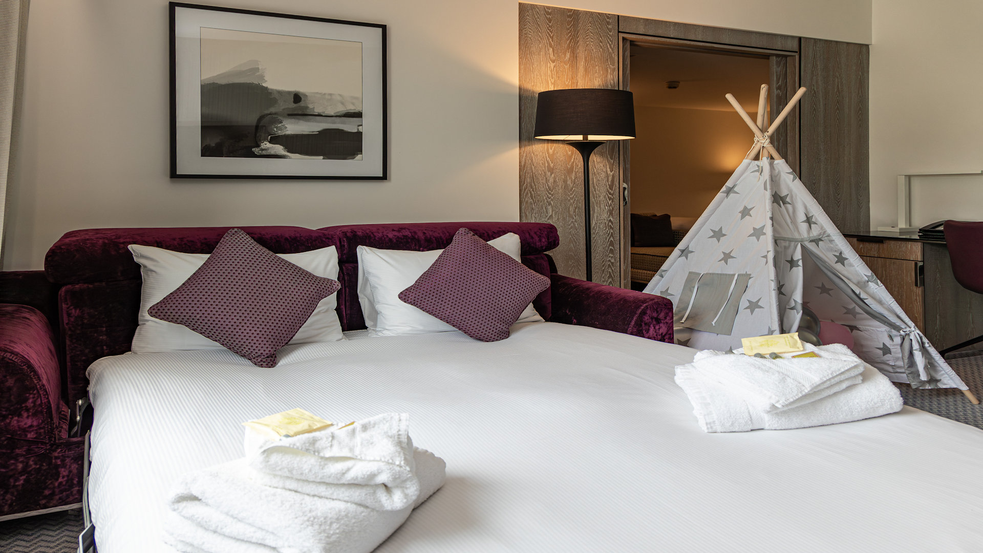 Hotel bedroom with double bed and child's teepee, bath robs on the bed 