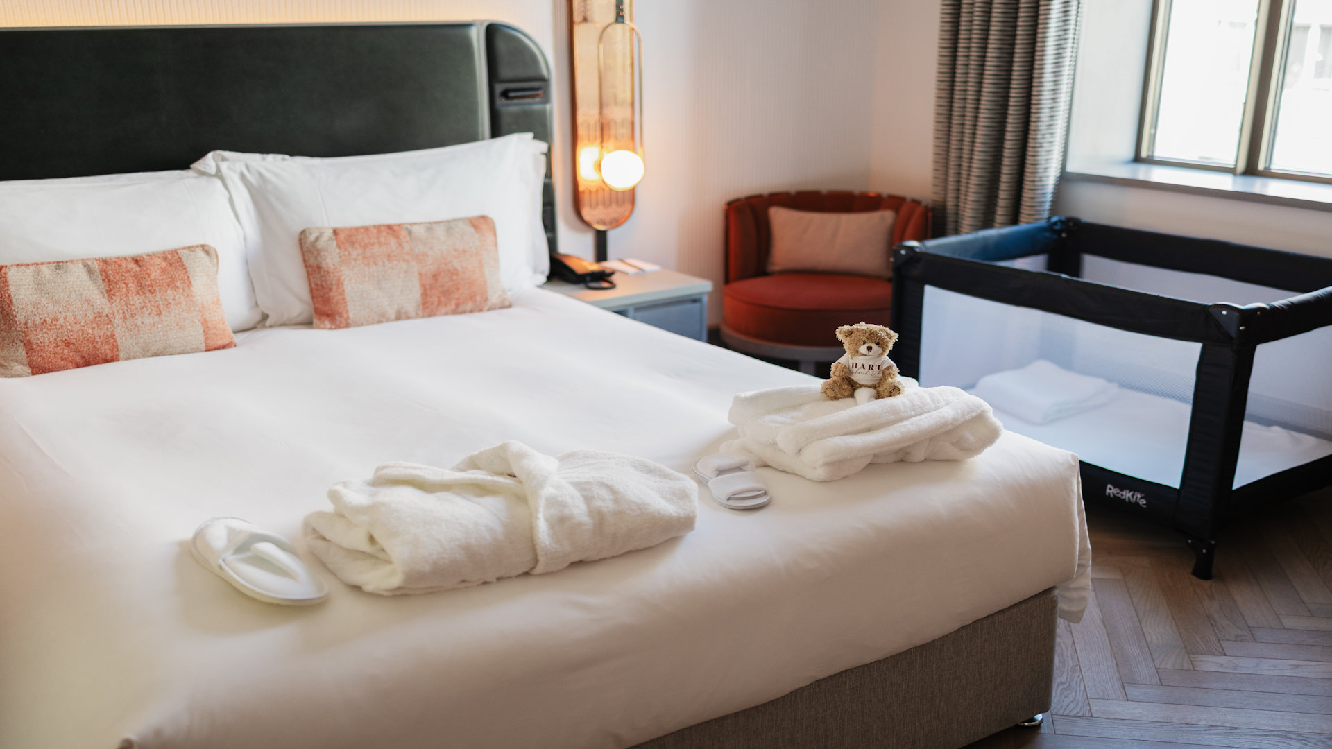 Hilton Hart Shoreditch Hotel family room. Image courtesy of Hilton. Family bedroom with large double bed, folded dressing gown and slippers on the bed, cot near the window