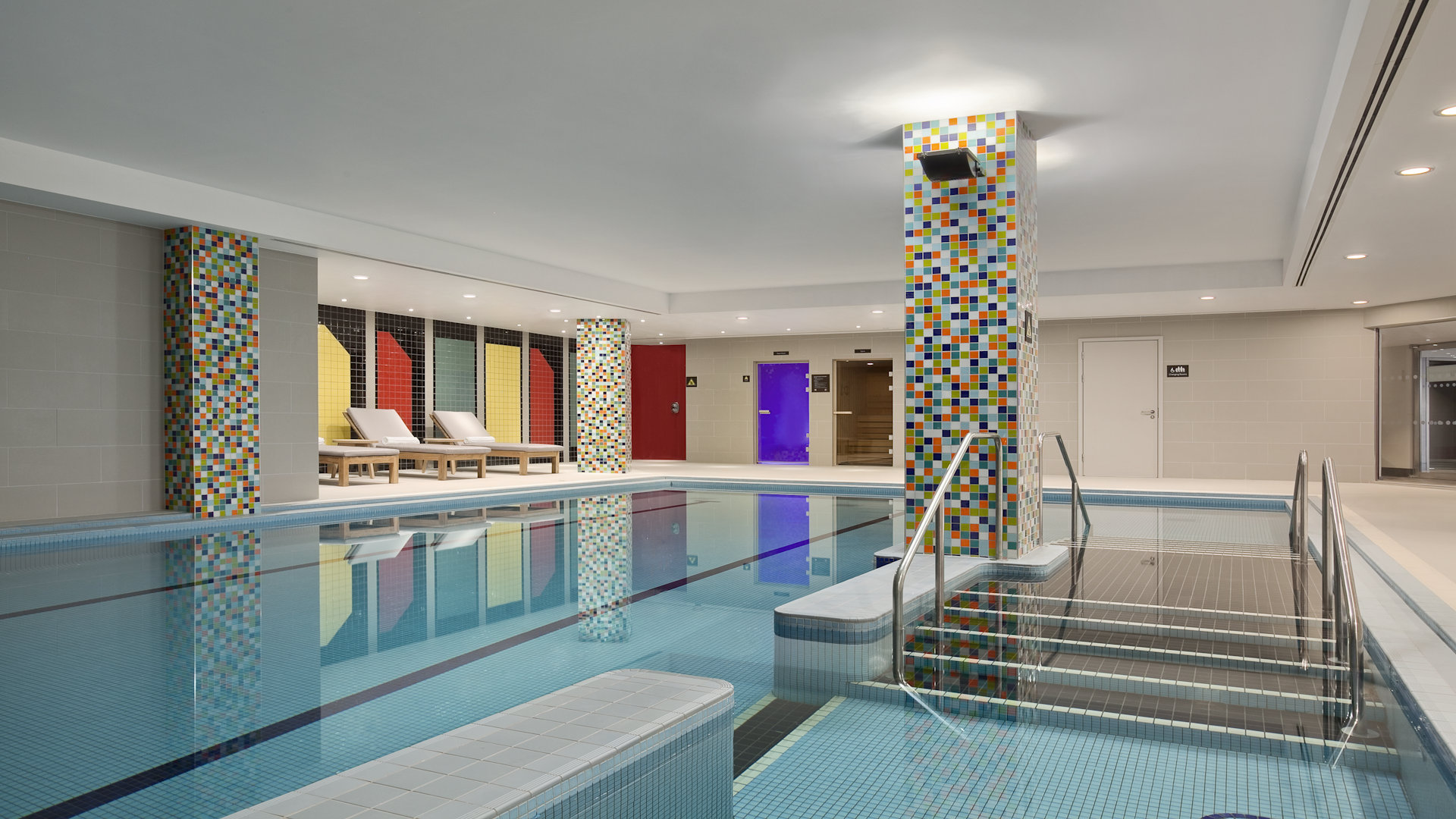 Indoor swimming pool with steps leading into the pool. Sun loungers on the side by the pool