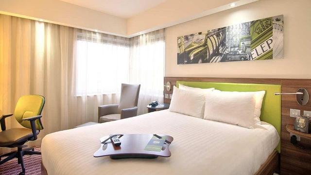 A bed with a lime green headboard, London-themed picture and a yellow chair.