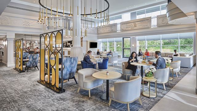 The Hilton London Croydon restaurant, decorated with grey carpet and assorted coloured chairs and tables, welcomes guests for afternoon tea.