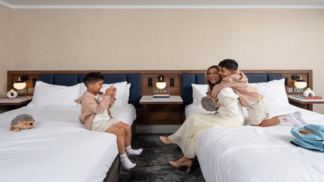 mother and child embracing on a bed, son taking a photo of them on the other bed 