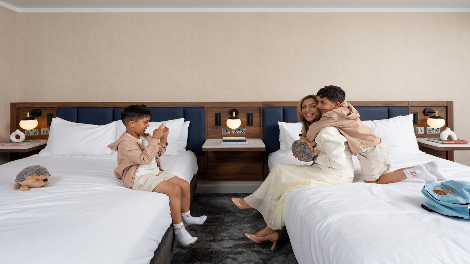 mother and child embracing on a bed, son taking a photo of them on the other bed 