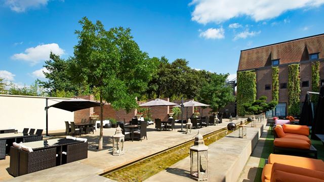 Outdoor terrace at Hilton Syon Park with tables, parasols, loungers and landscaped greenery.