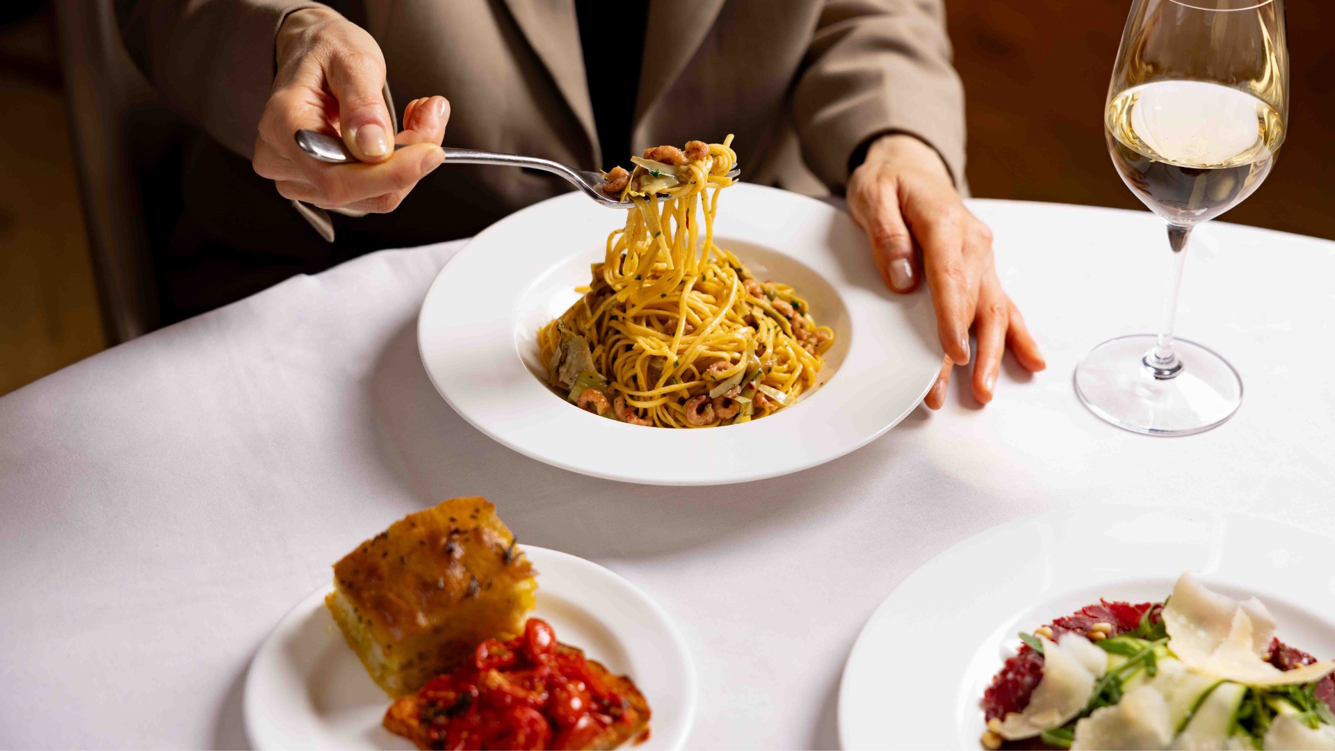 Several dishes on a table with white tablecloth, including a spaghetti dish, with someone tucking into it.