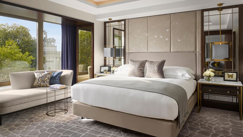 Enjoy sweeping views of Wellington Arch and Hyde Park. Credit: InterContinental London Park Lane. Image courtesy of InterContinental London Park Lane. Luxury hotel room with white and grey bedding and cushions, grey carpet, sofa and floor-to-ceiling windows overlooking Hyde Park on a sunny day.