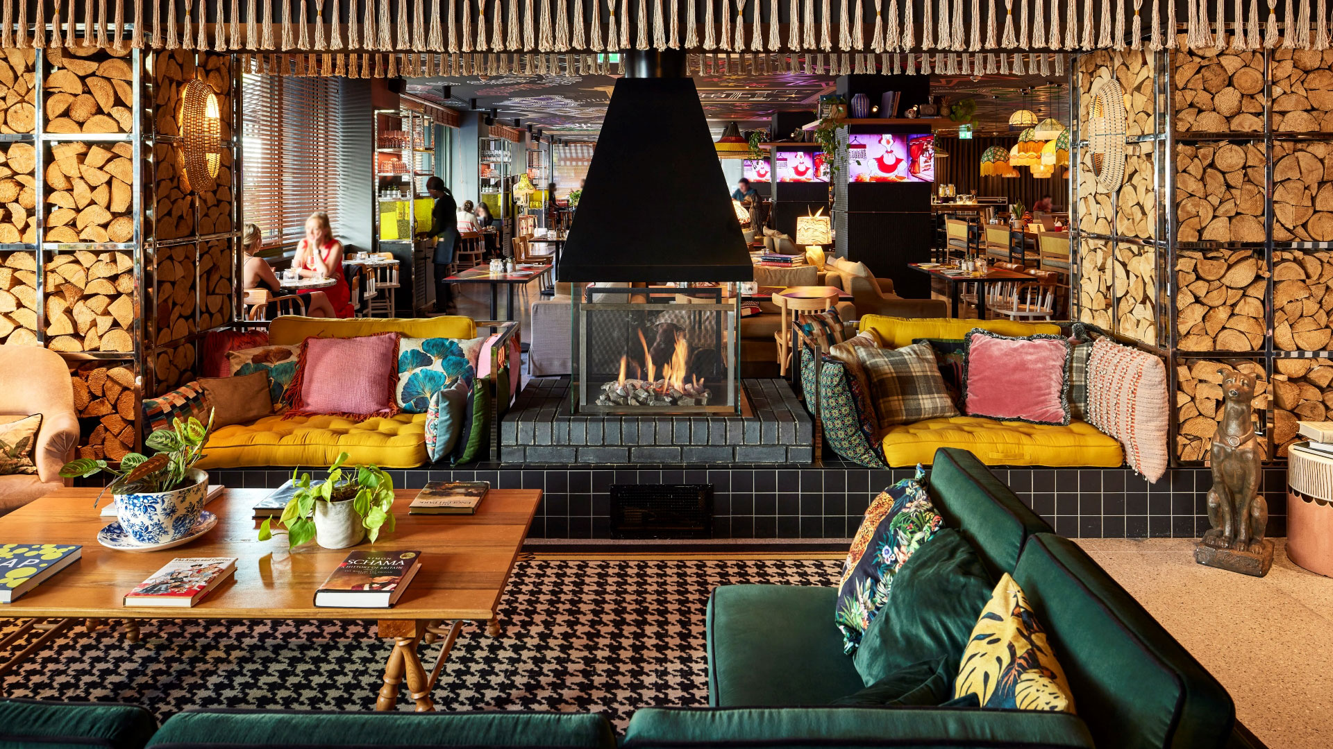 The colourful lounge at Mama Shelter featuring a log fireplace, quirky carpets and teal velvet sofas