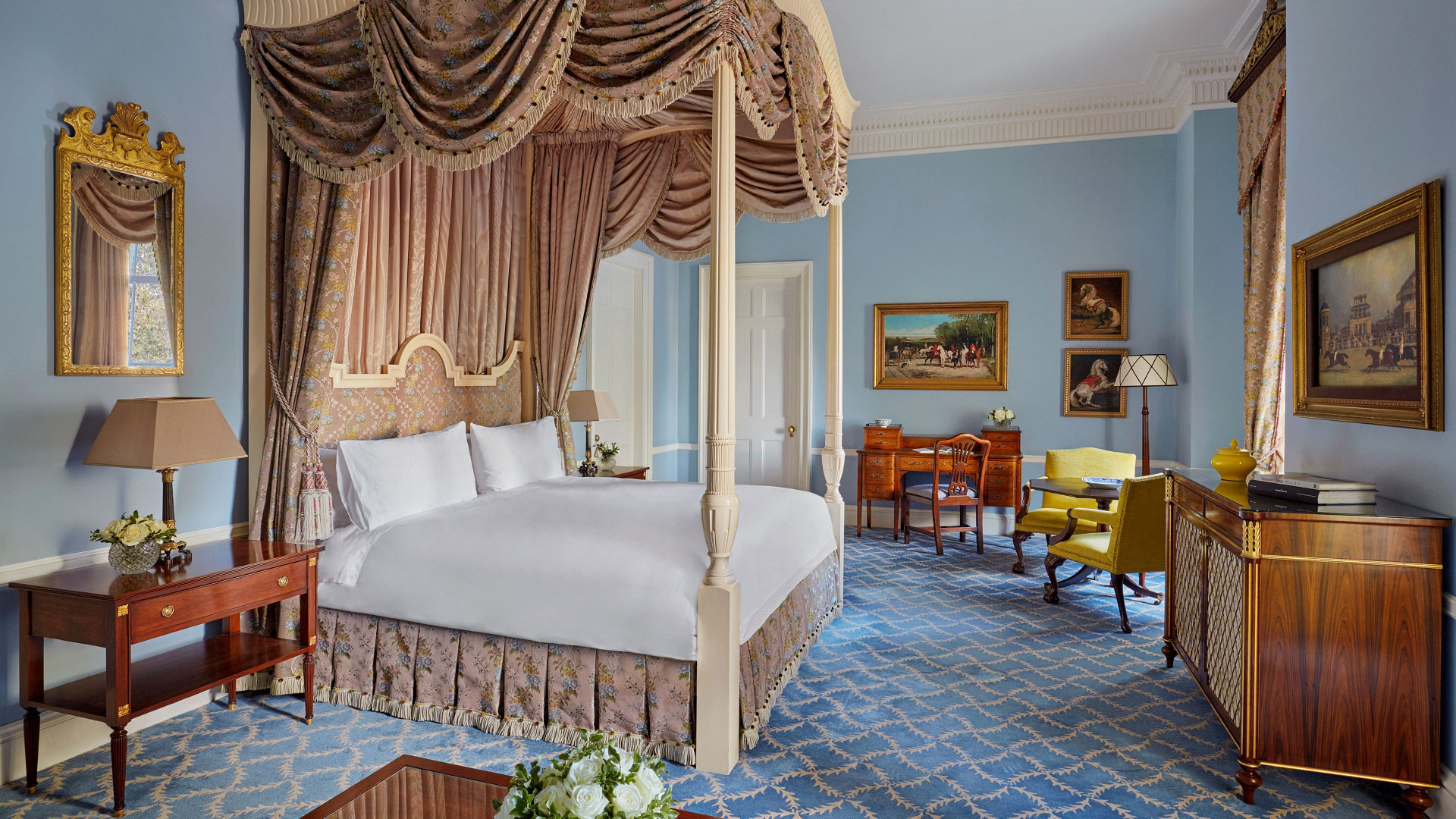 a four poster bed with golden gathered framing stands in the middle of a room lined with dark wooden furniture and gold framed paintings
